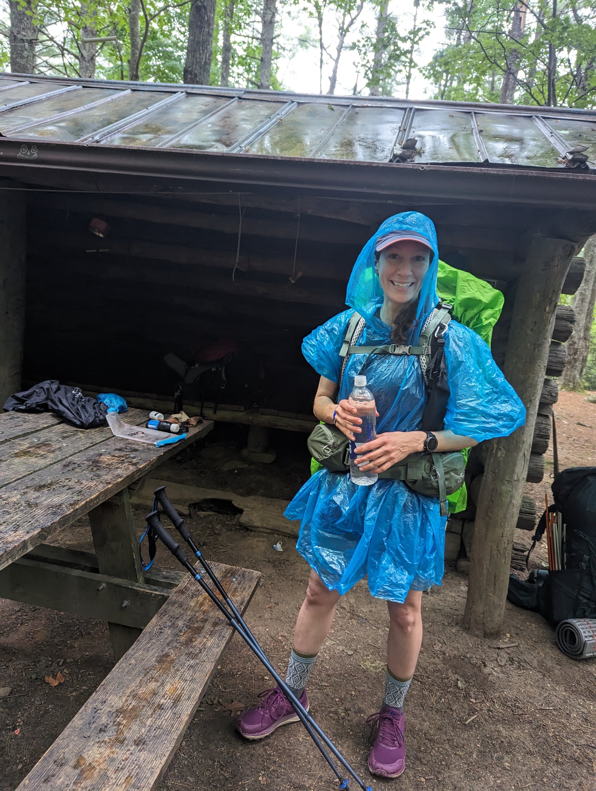 A woman wearing a poncho and a backpacking standing in front of a wooden shelter on the Appalachian Trail
