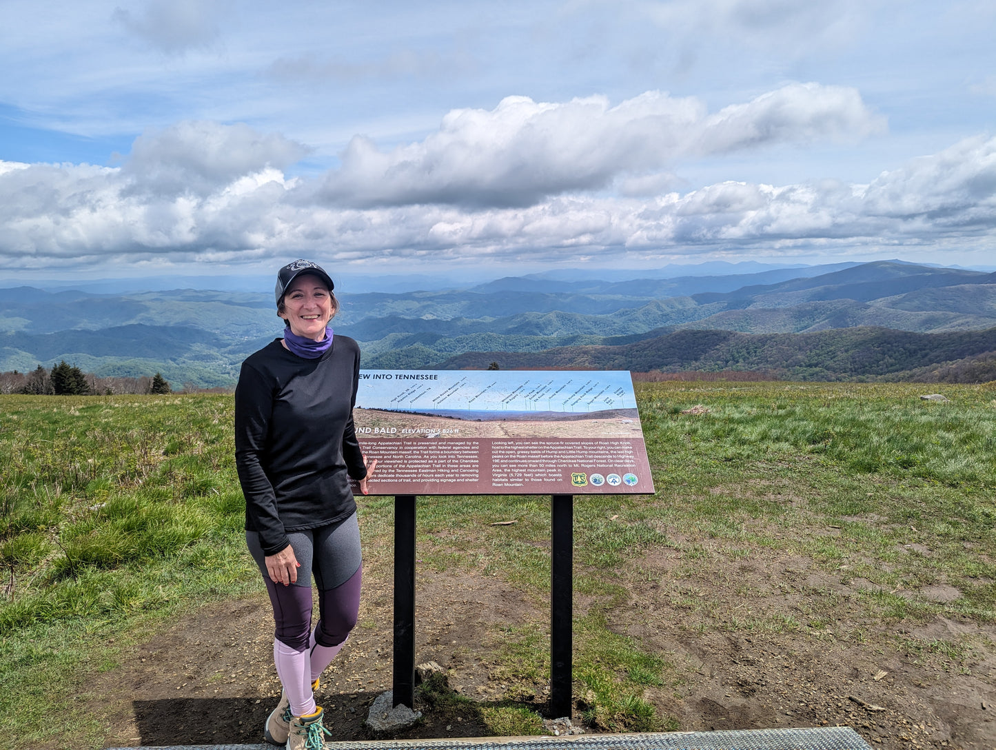 A woman standing in front of a sign on the summit of Round Bald