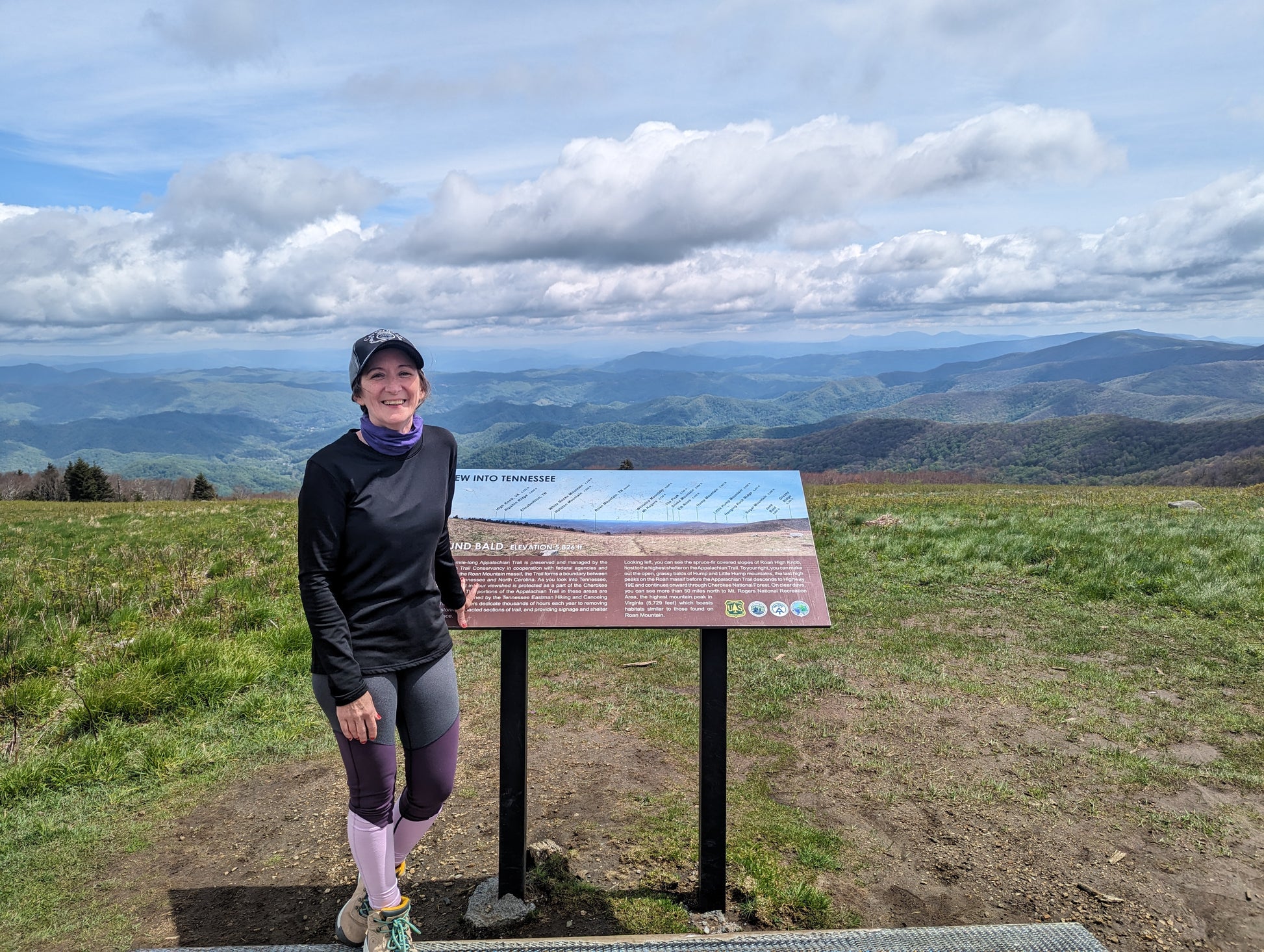A woman standing in front of a sign on the summit of Round Bald