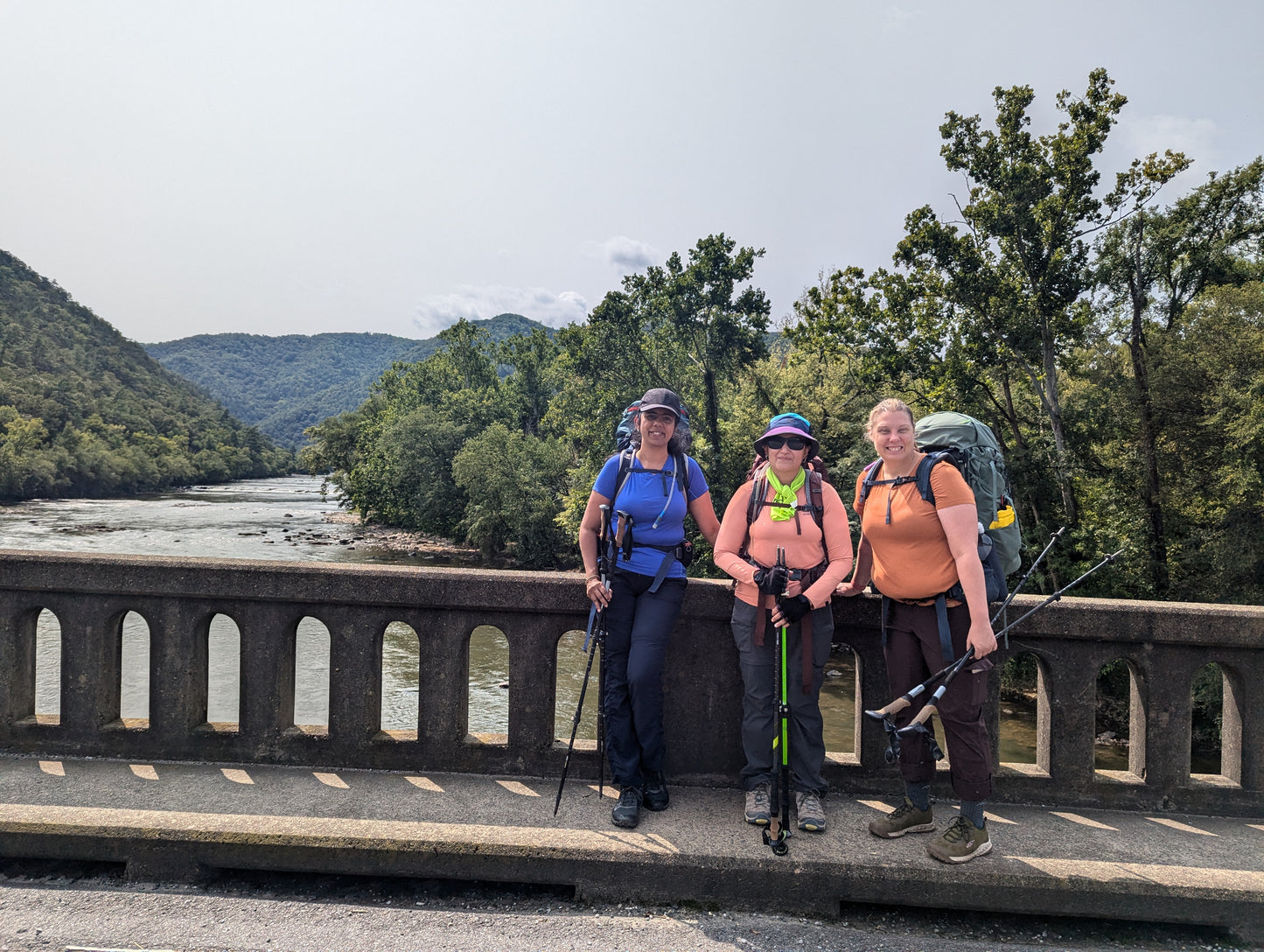 Three women with backpacks standing on a bridge over the French Broad River on the Appalachian Trail