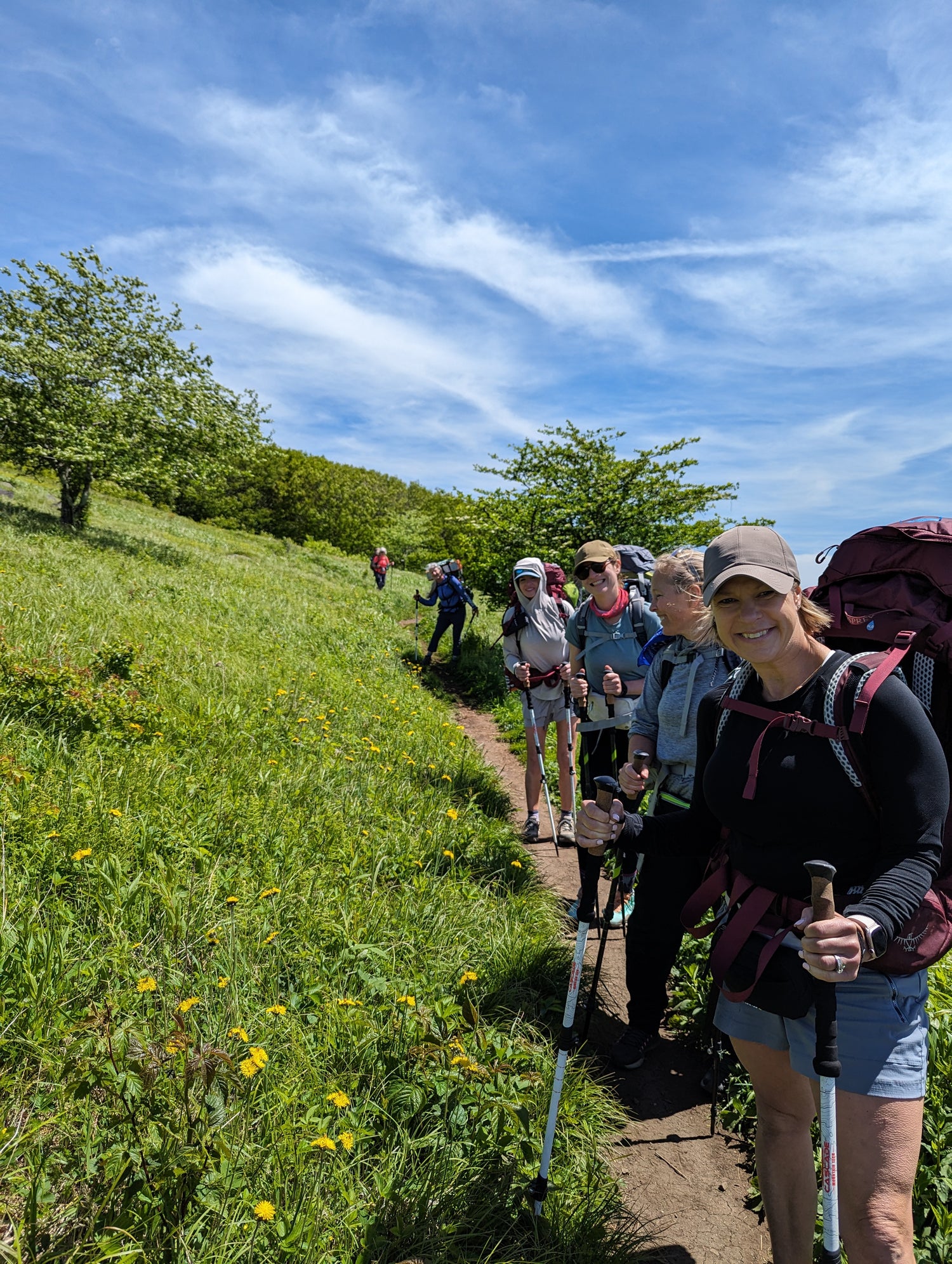 Six women standing on a hiking trail with backpacks and trekking poles