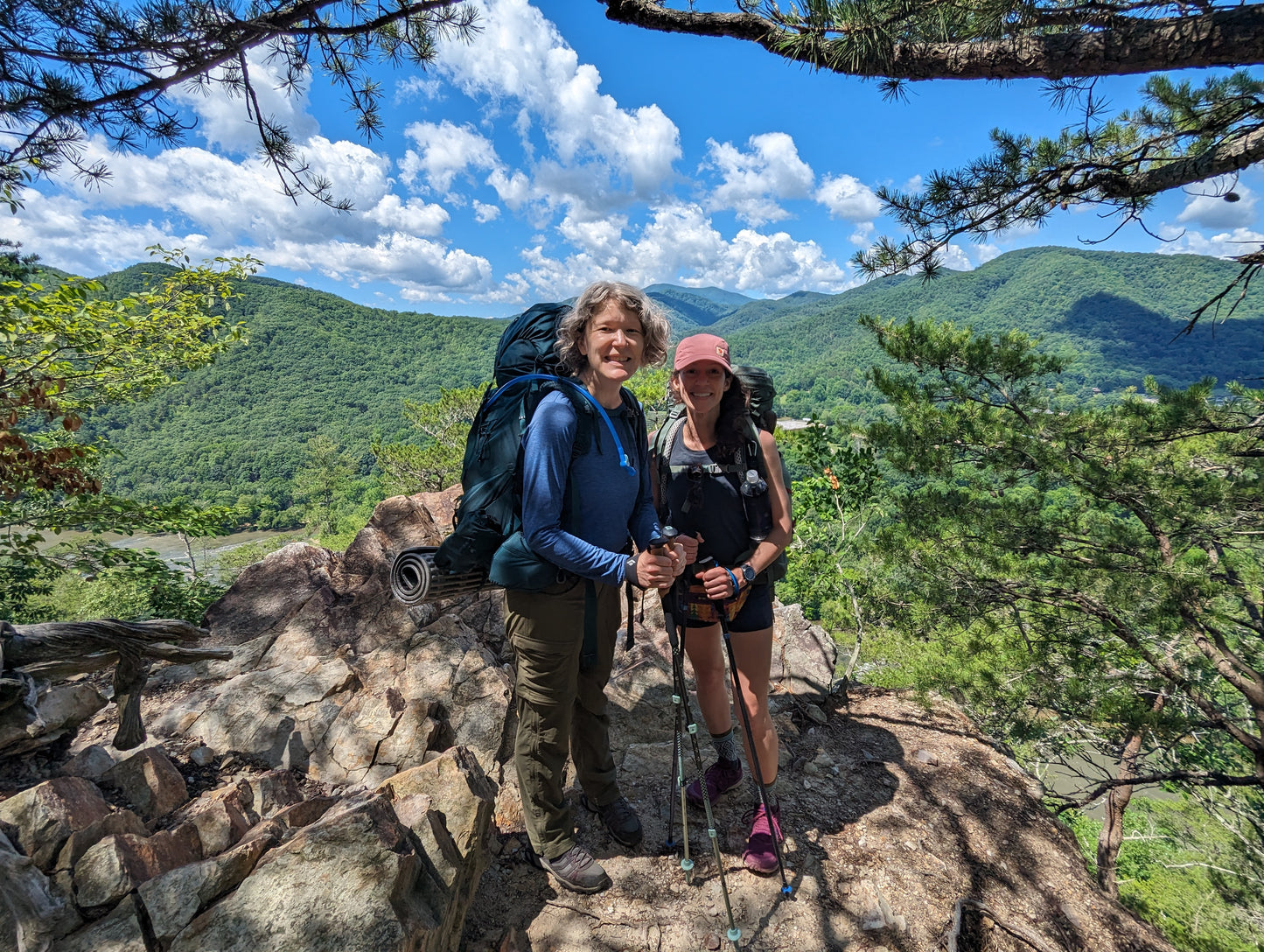 Two woman with backpacks standing on a rocky outcropping overlooking the French Broad river below