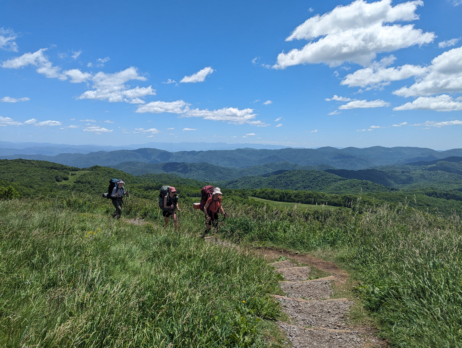 Three women wearing backpacks as they hike on the Appalachian Trail with mountains in the background